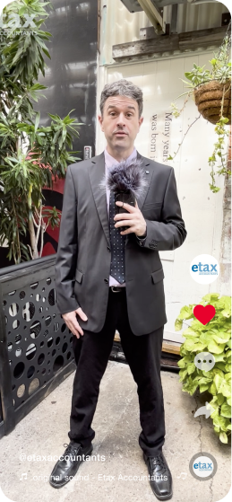 A man in a black suit stands outdoors holding a microphone. He is surrounded by plants and industrial items. There are icons on the right side of the image indicating that it is a social media video, and a username "@etaxaccountants" is visible in the bottom left corner.