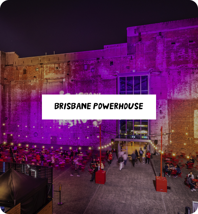 Brisbane Powerhouse at night, with purple lighting on the brick facade and people sitting at outdoor tables in a lively, illuminated courtyard.