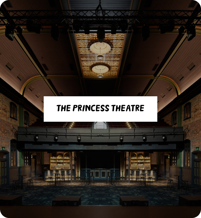 The interior of The Princess Theatre featuring ornate lighting, high ceilings, exposed brick walls, a stage, and bar area, with a white sign in the center reading "The Princess Theatre.