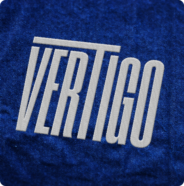 The word "VERTIGO" is written in tall, white, bold letters on a textured blue background. The "V" and "T" are especially elongated.