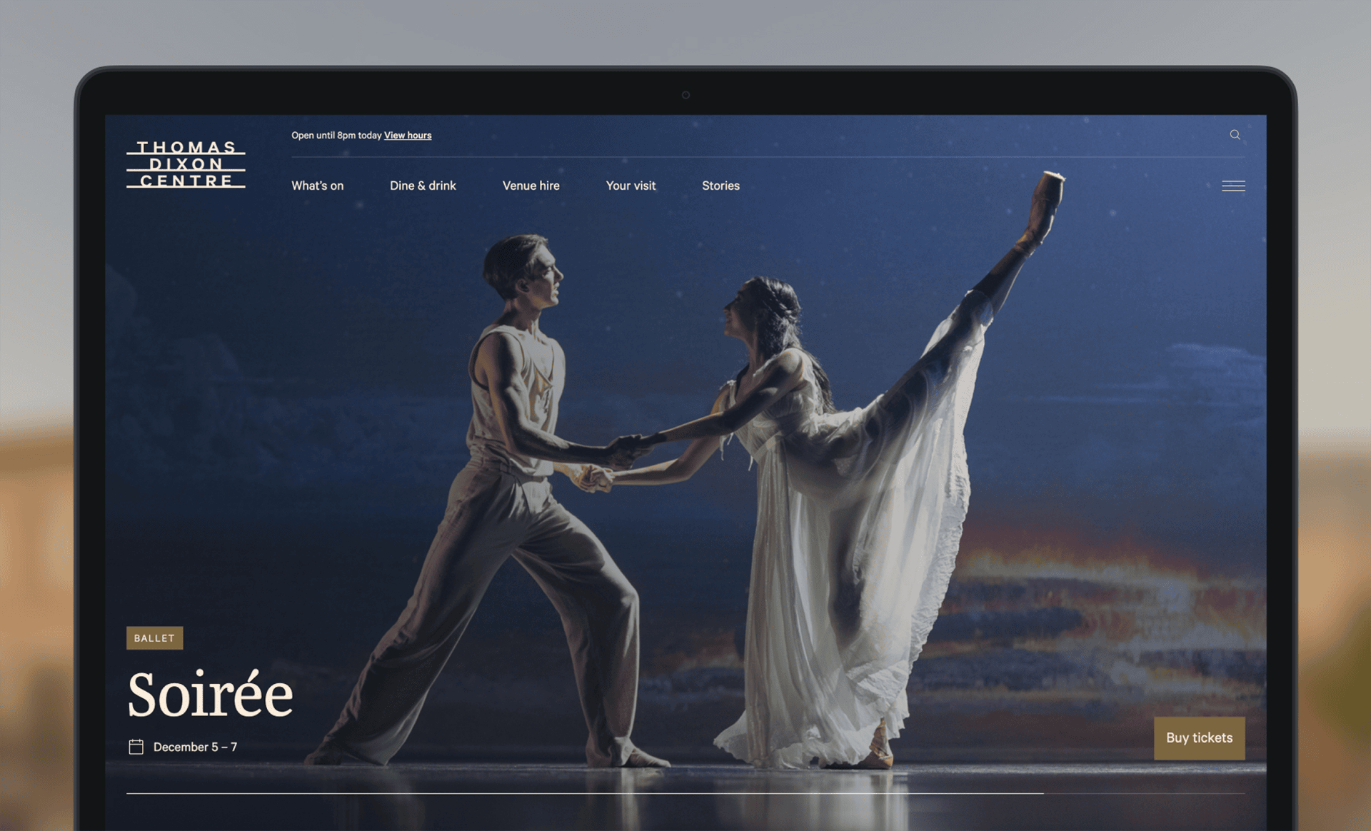 A laptop screen displays the Thomas Dixon Centre website, featuring ballet dancers performing on stage with text promoting the event "Soirée," taking place December 5–7, and a button to buy tickets.