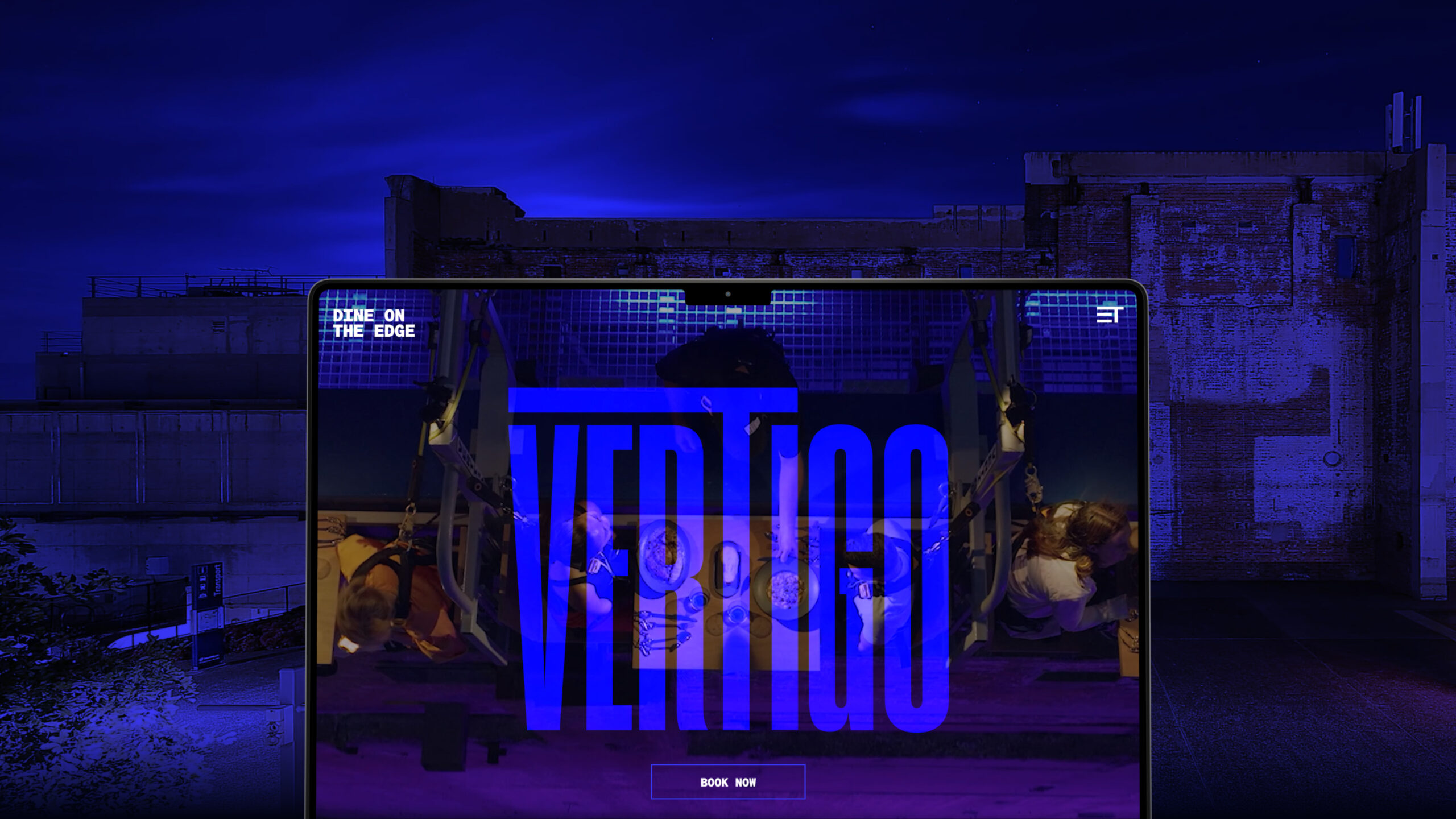 A digital screen displays the word "VERTIGO" in bold blue letters, with two people seated in harnesses. The background shows an urban rooftop at night with blue lighting.