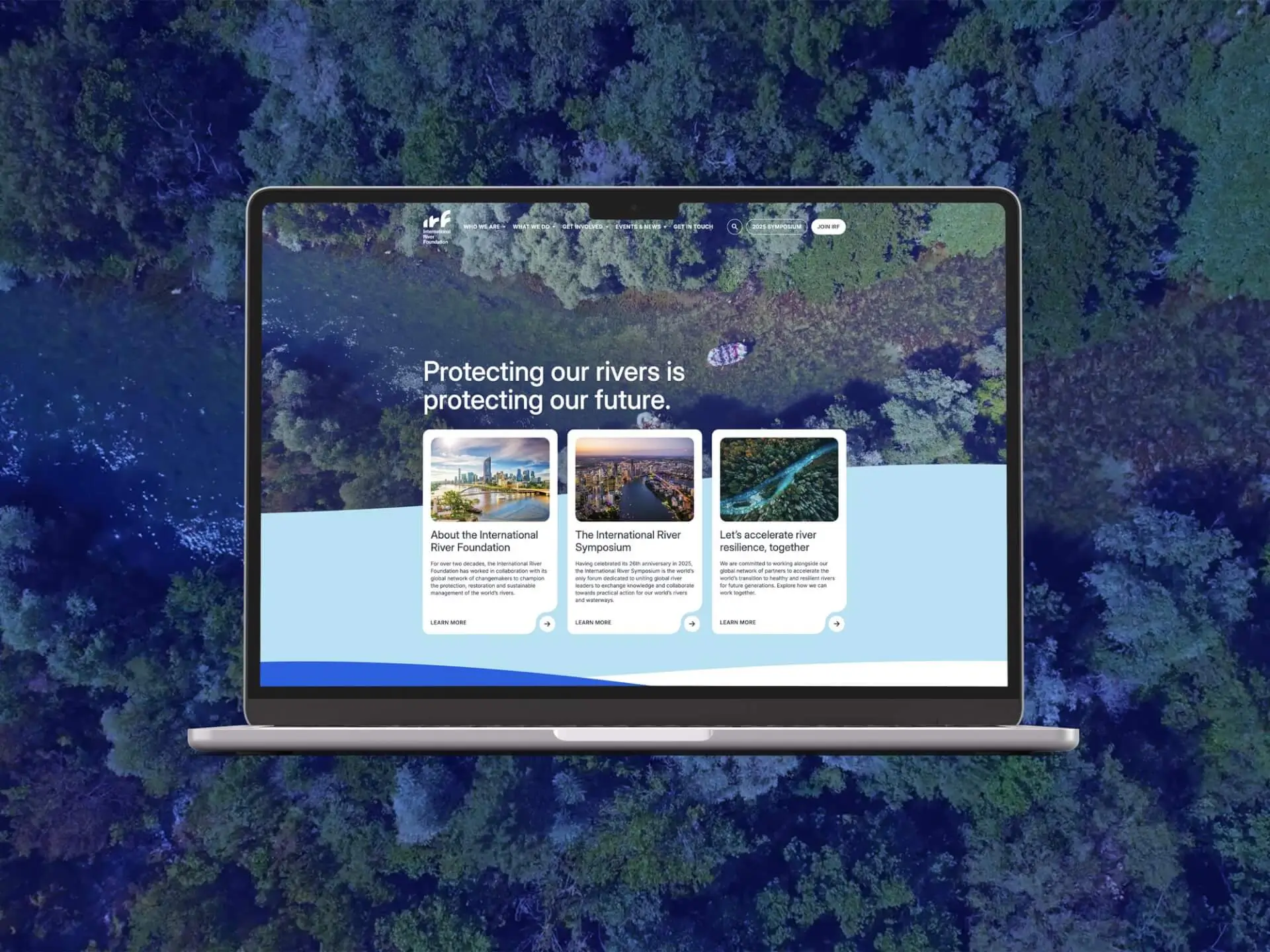 A laptop displays a website with the headline "Protecting our rivers is protecting our future" over a river background, featuring river conservation projects. The laptop is set against an aerial view of a forest and river.