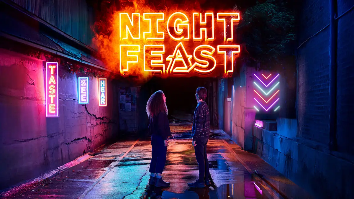 Two people stand facing each other in a neon-lit alley at night. Bright signs say "NIGHT FEAST," "TASTE SEE HEAR," and neon arrows. The ground is wet, reflecting the colorful lights.