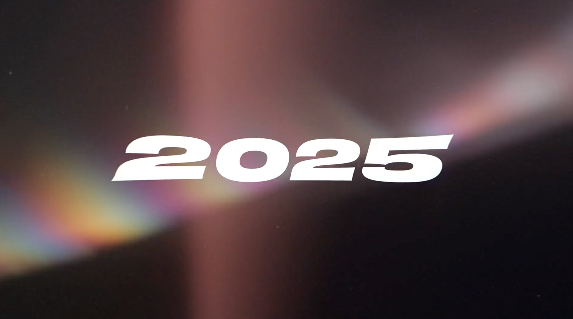 Bold white text reading "2025" appears in the center of a dark background with a soft, colorful light flare and gradient effect.