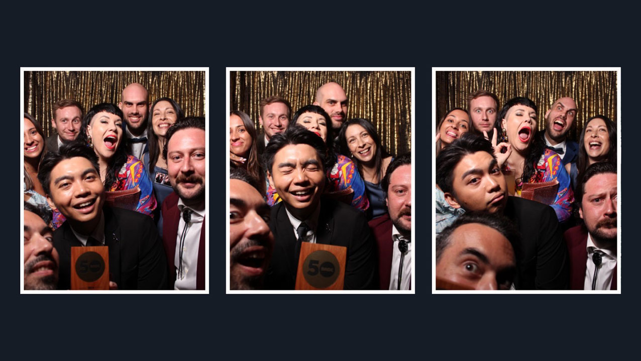 People posing in a photo booth with a 50 award sign