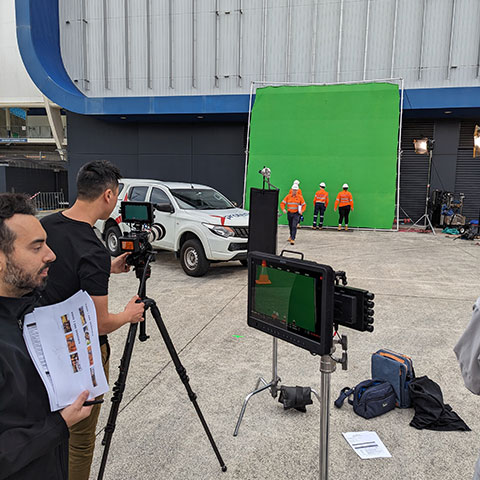 Film crew recording workers near a green screen