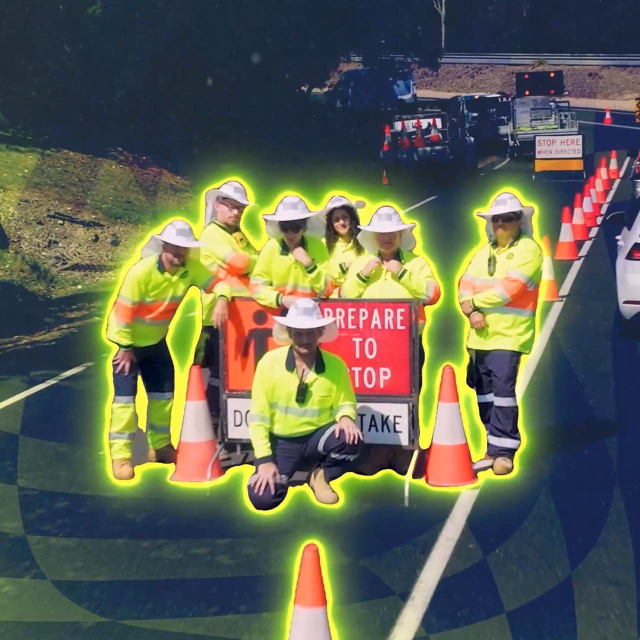 A group of road workers in neon yellow safety jackets pose around a "Prepare to Stop" sign beside traffic cones on a road, with vehicles and more cones visible in the background.